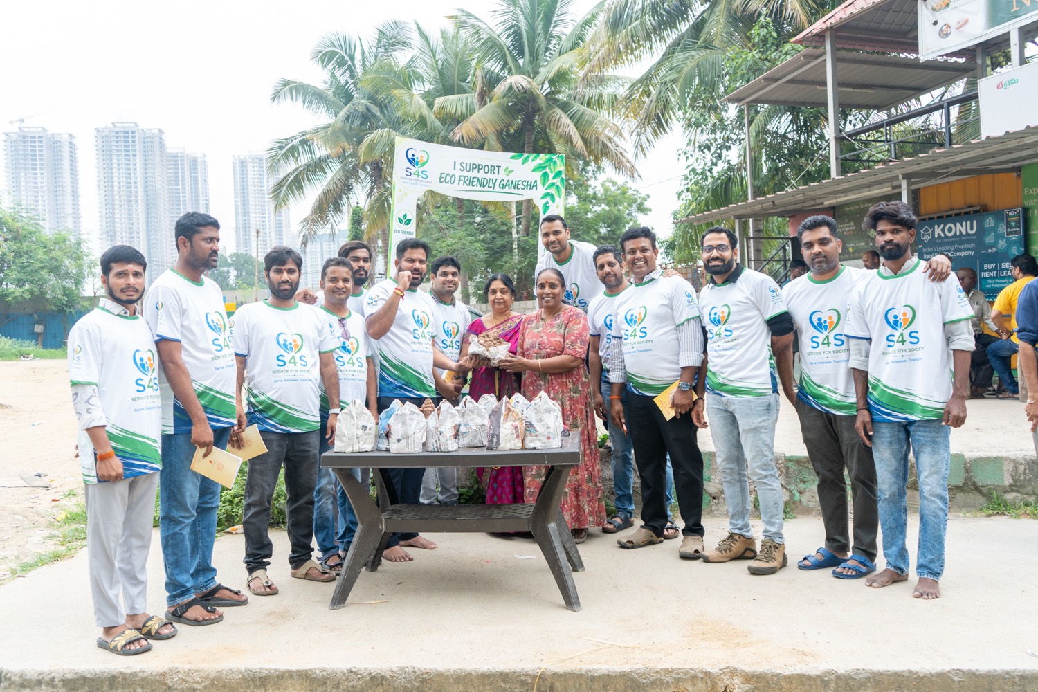Volunteers and residents at a table of clay Ganesha idols under an I Support Eco Friendly Ganesha banner