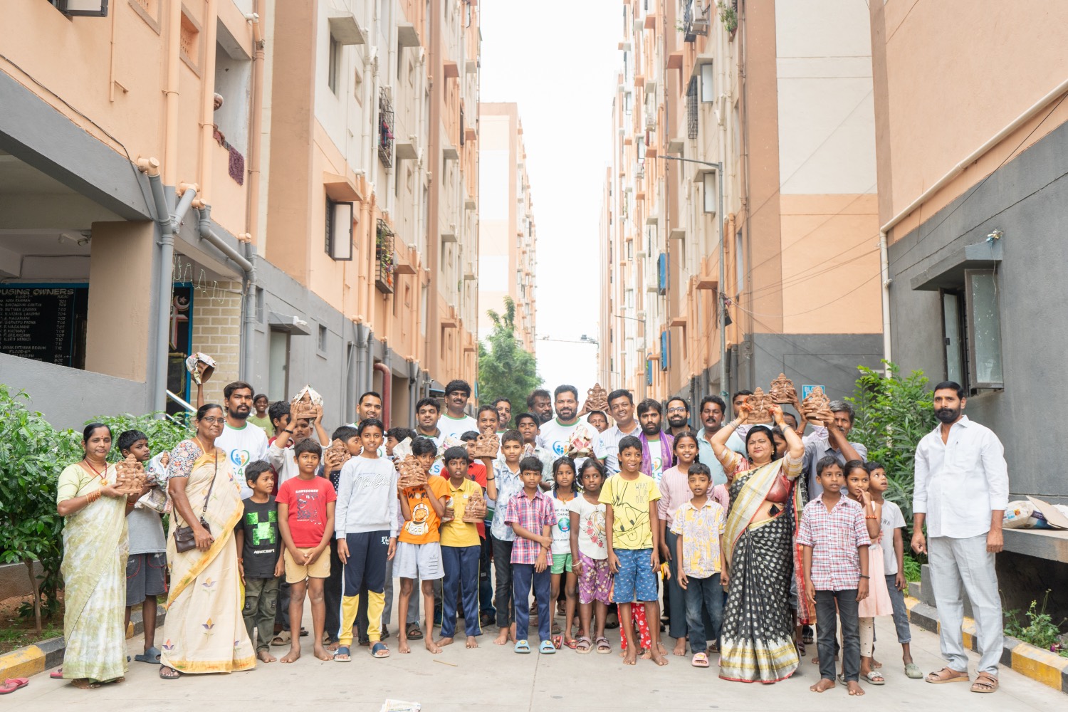 Children and residents holding clay Ganesha idols on a street between housing blocks